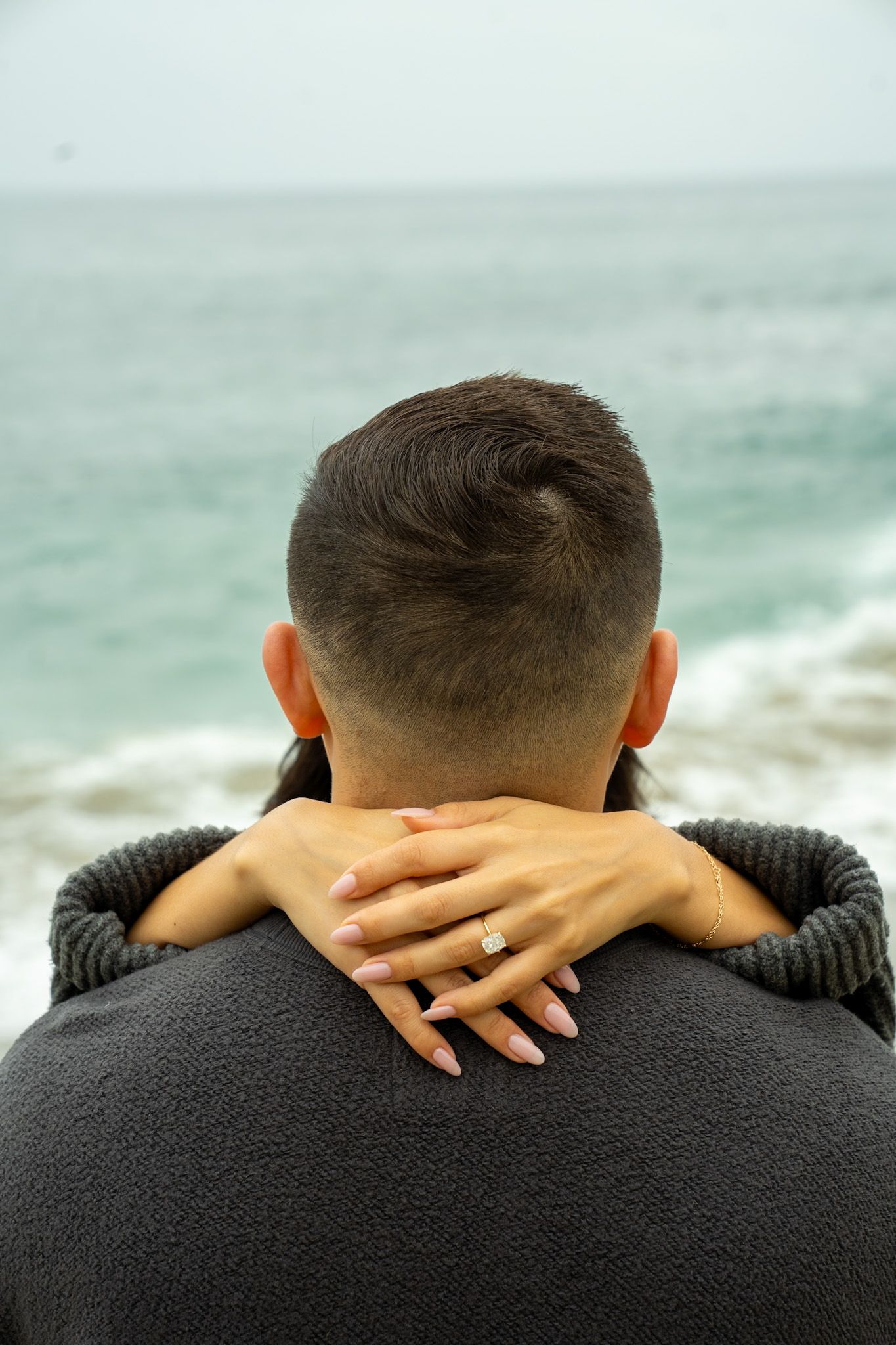 A close-up view of hands resting on shoulders with a misty ocean backdrop.