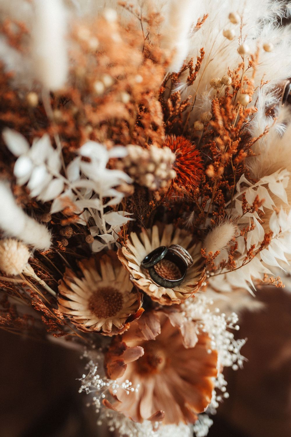 detail photo of wedding rings placed on dried floral bouquet at intimate wedding in Boone Iowa
