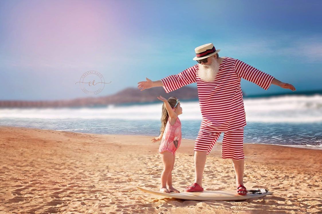 Two figures playing and posing with outstretched arms on a sunny beach.