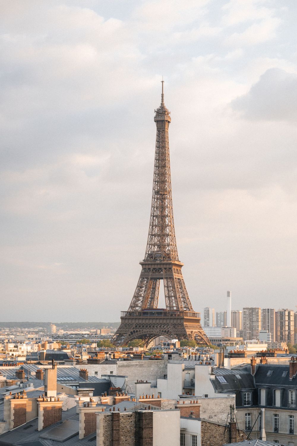 View of the iconic Eiffel Tower rising above Parisian rooftops and buildings during sunset.