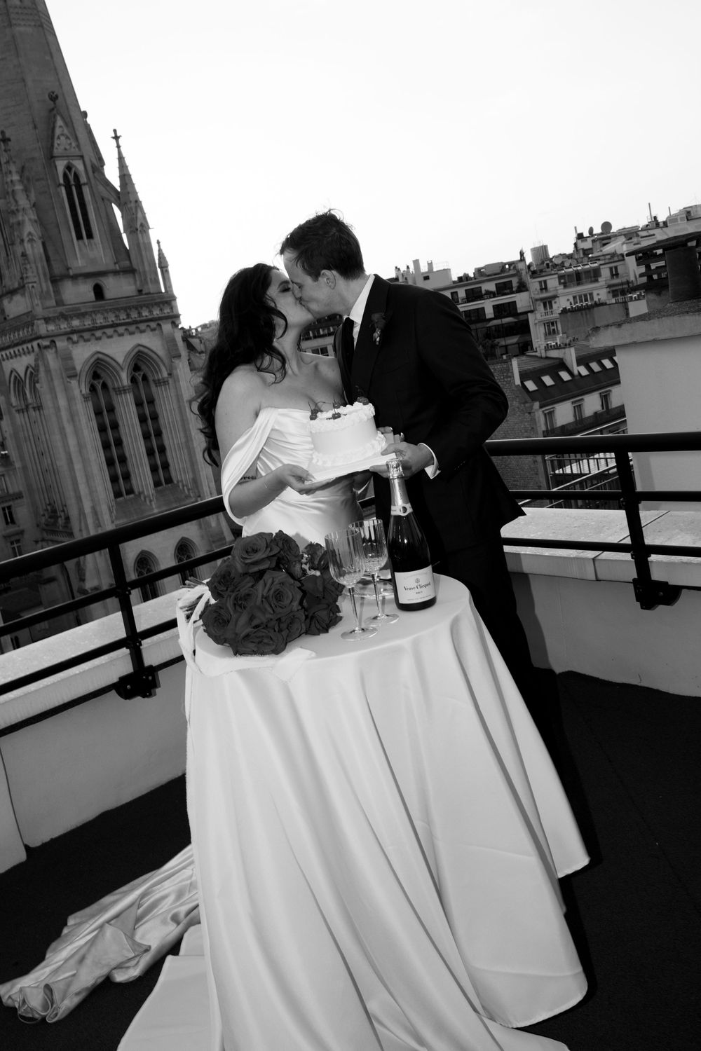 Romantic black and white photo of newlyweds sharing a moment at a table on a Parisian rooftop.
