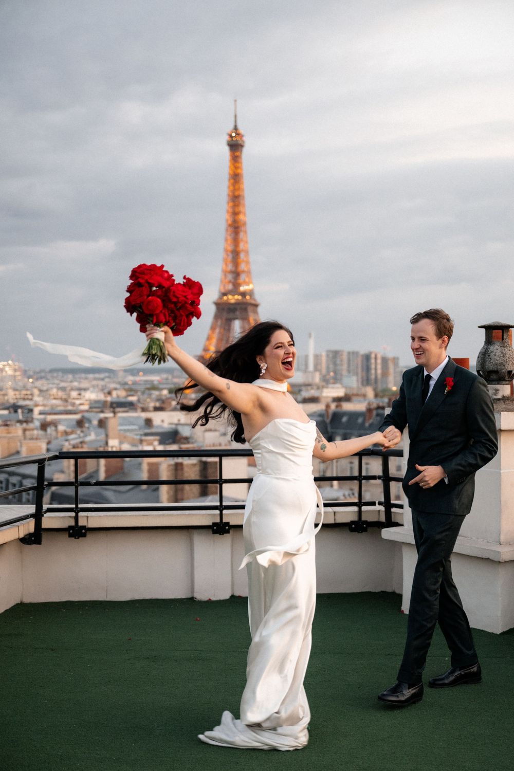 A romantic wedding moment on a Paris rooftop with the illuminated Eiffel Tower glowing in the background at dusk.