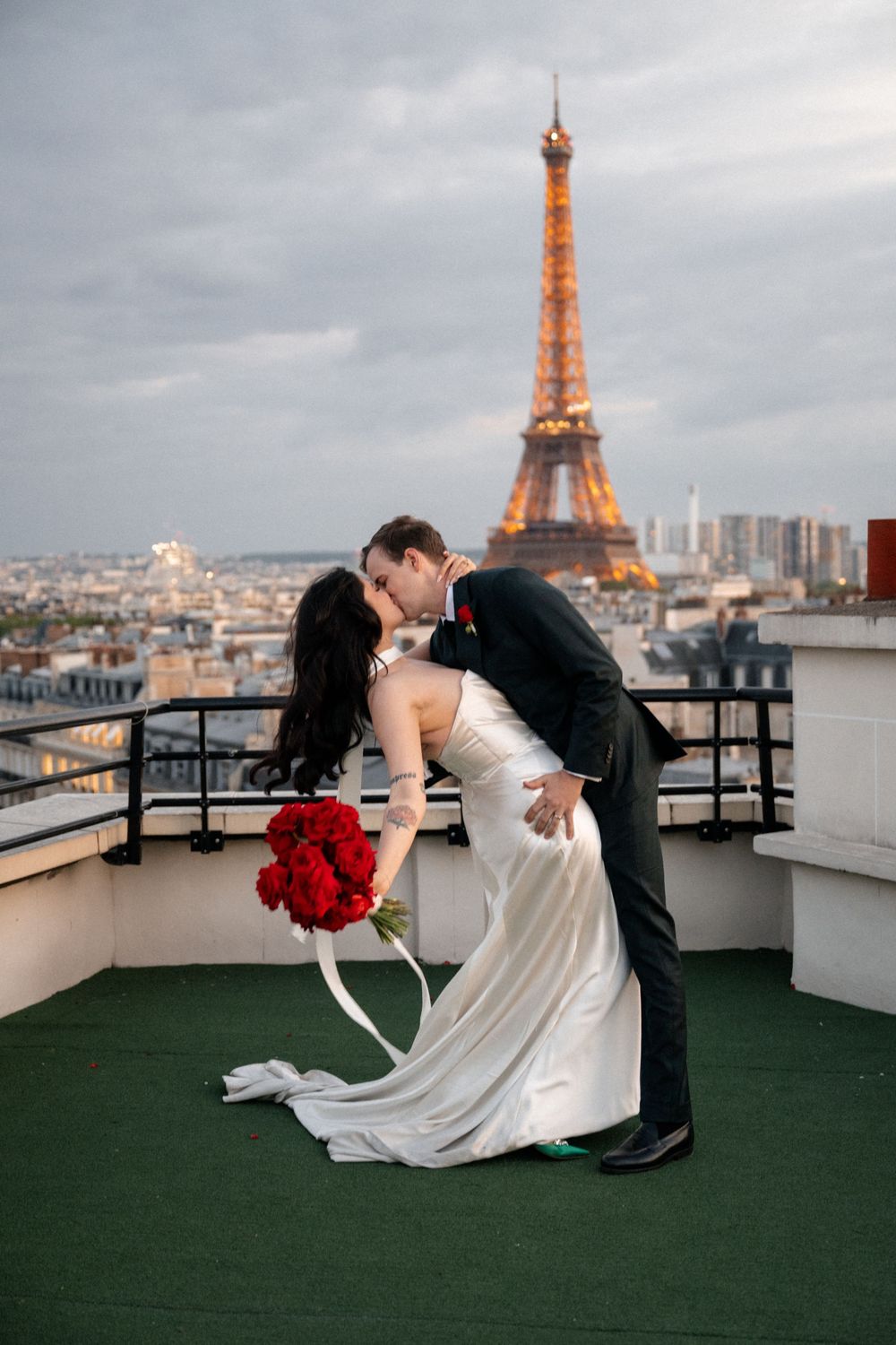 Romantic wedding couple dips and kisses on a rooftop terrace with the iconic Eiffel Tower glowing in the Paris skyline.