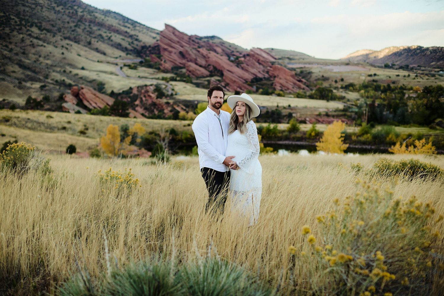 Expectant couple embracing in field at sunset during maternity session in Morrison Colorado