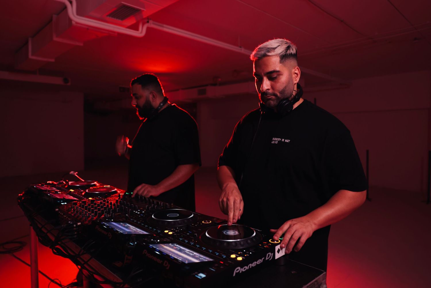DJs performing with electronic equipment under dramatic red stage lighting.