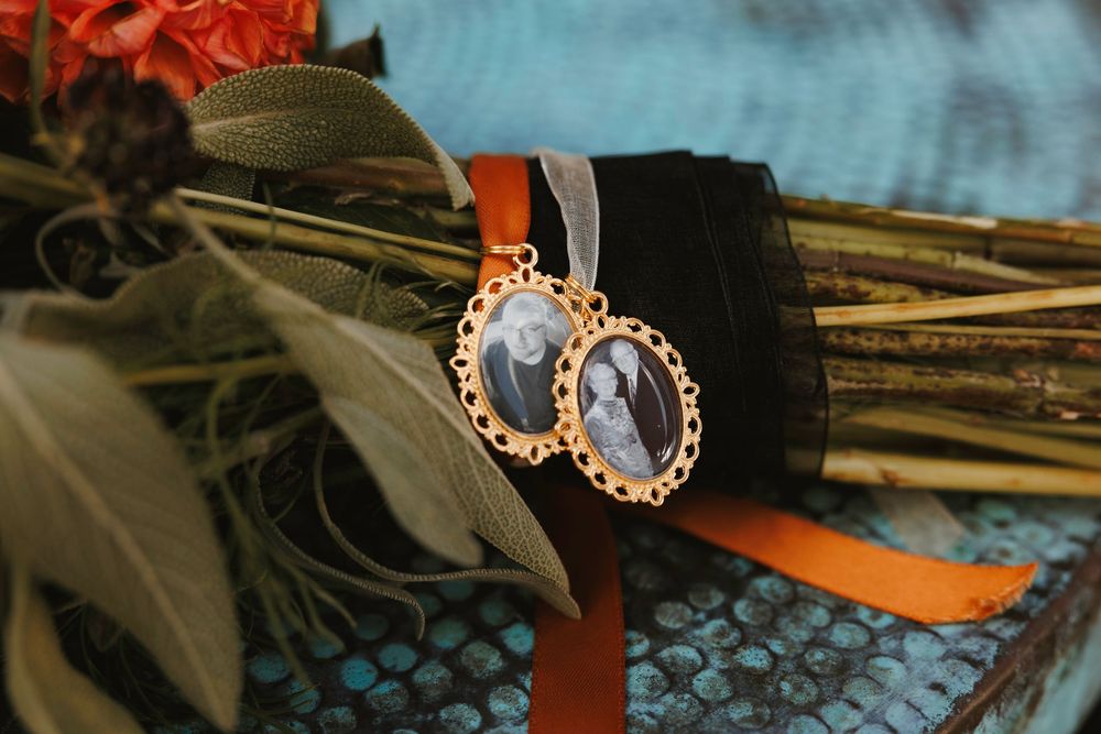 Gold oval memorial photo charms tied with orange ribbon to bridal bouquet stems.