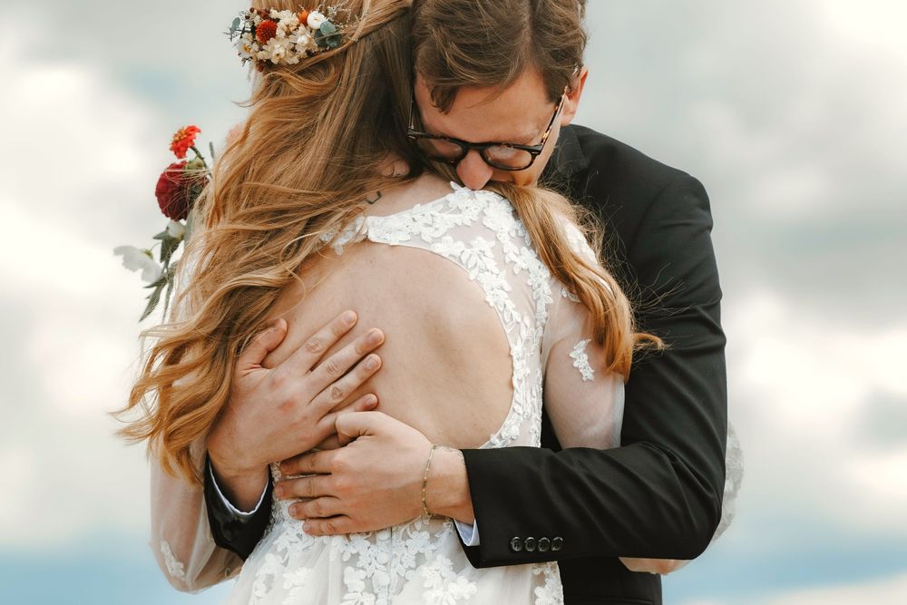 Emotional bride and groom sharing a close embrace under a dramatic cloudy sky.