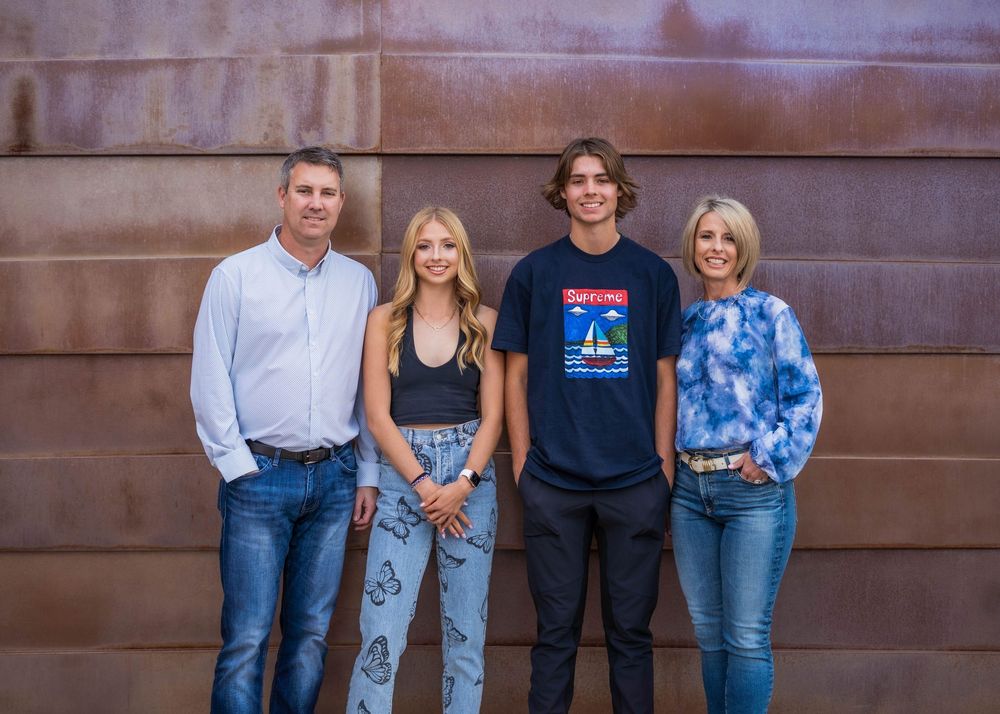 Family members in coordinated blue and black outfits pose together against a rustic brown wall background.