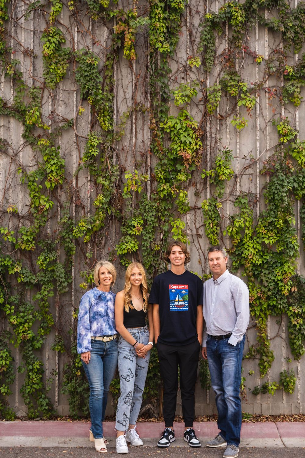 A family group stands against a wall covered in climbing green ivy vines.