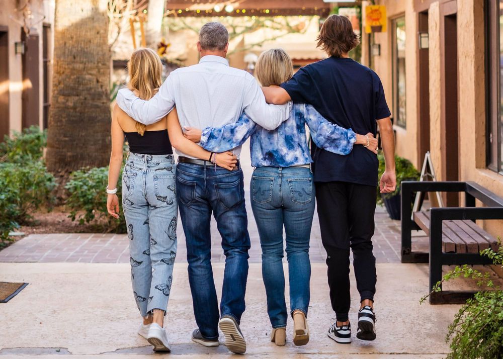 A family of four walking together arm in arm down a street at sunset.
