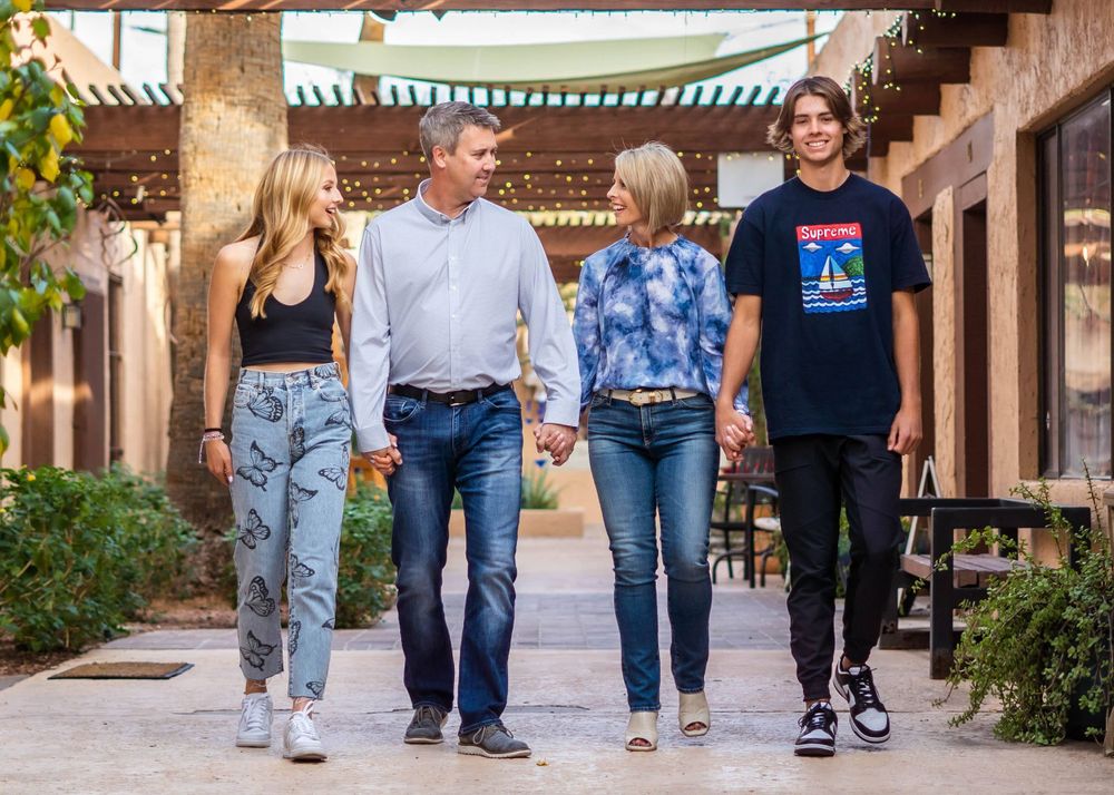 A family walks together holding hands on a pathway with Spanish architecture.