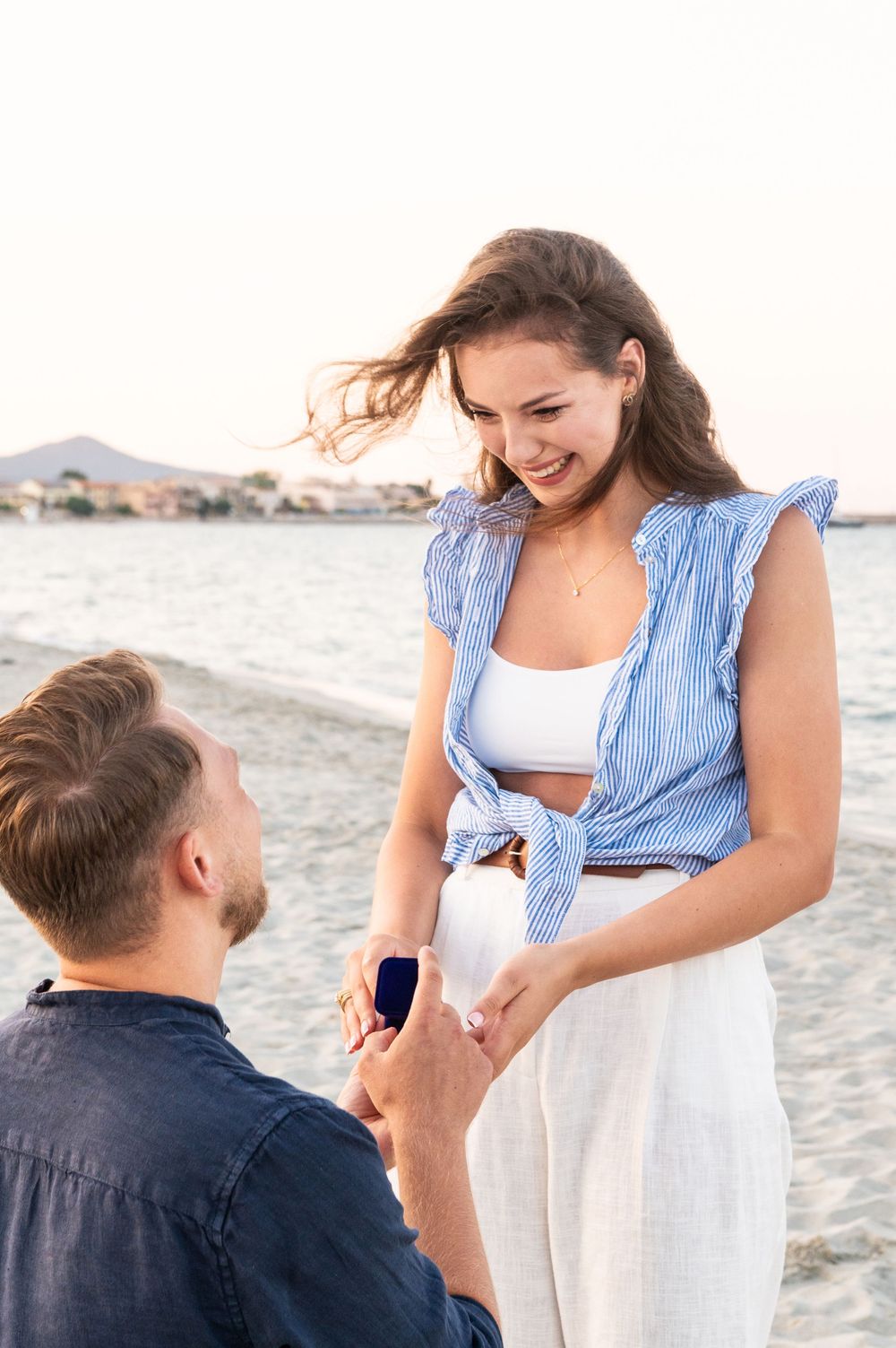 A proposal moment on a beach with the ocean in the background.