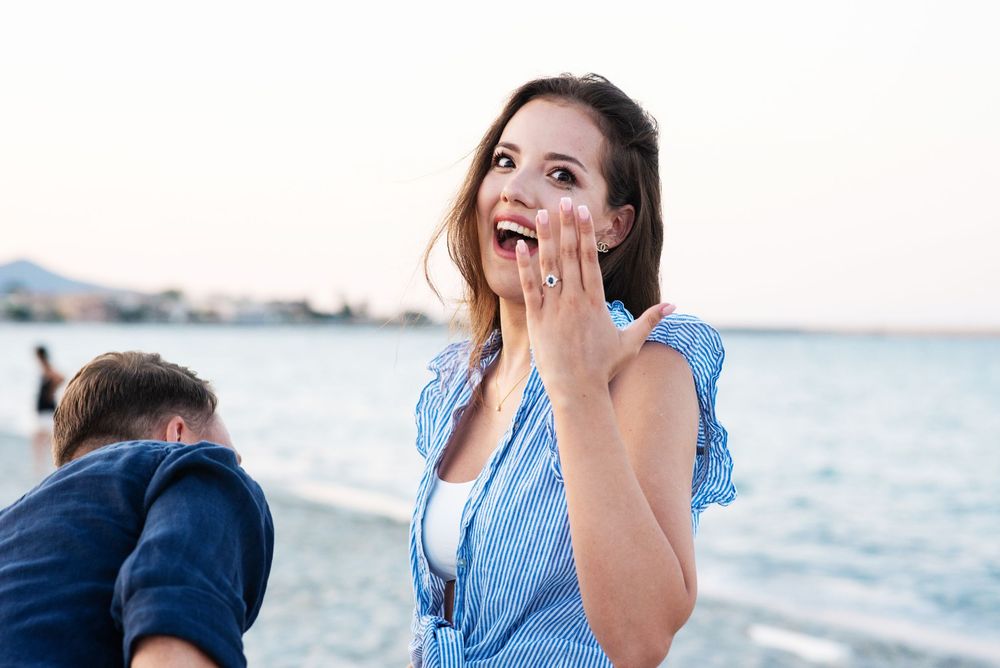Joyful reaction during a surprise beach proposal with ocean in background.