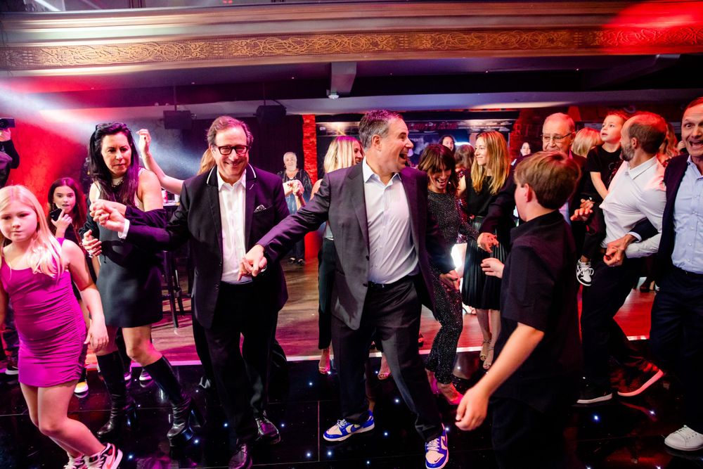 Energetic crowd dancing and celebrating at a nightclub event with red lighting.