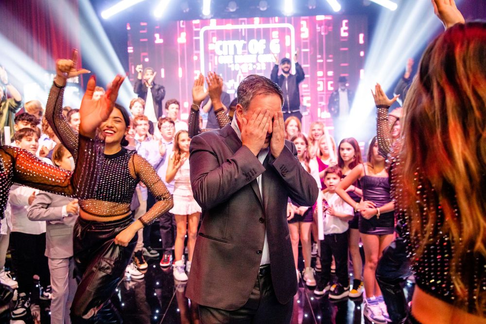Crowd celebrates at a nightclub with dramatic spotlights and stage effects in the background.