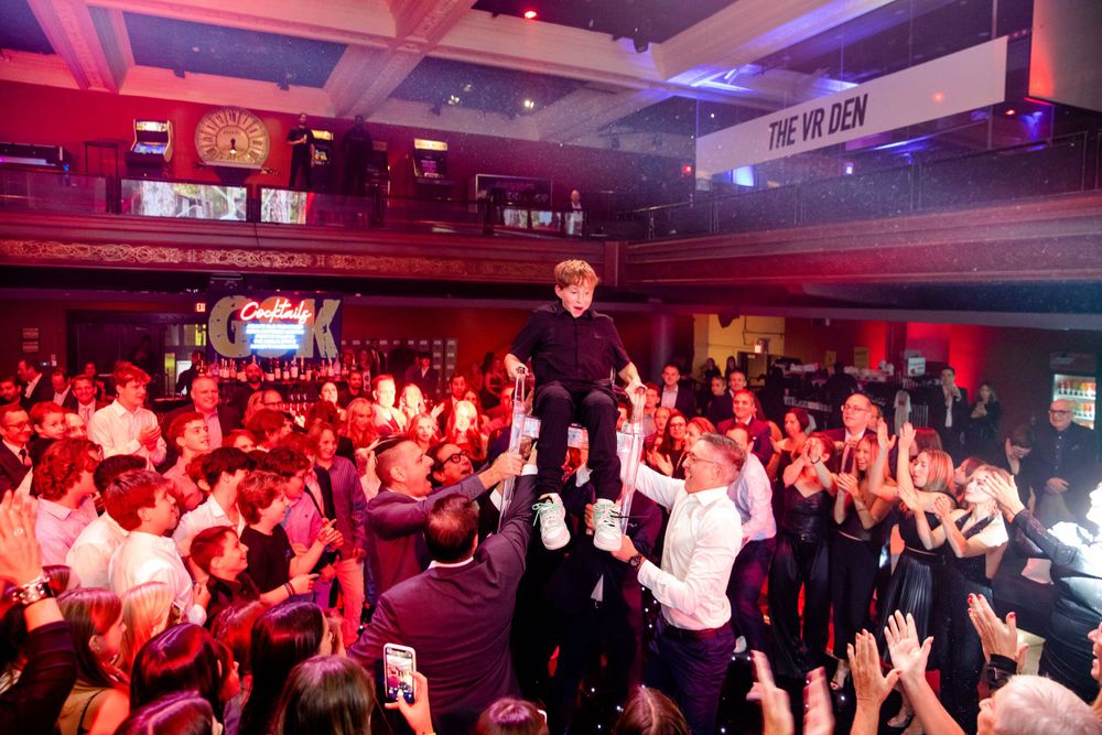 Crowd surfing moment during an indoor concert with dramatic pink and red lighting effects.