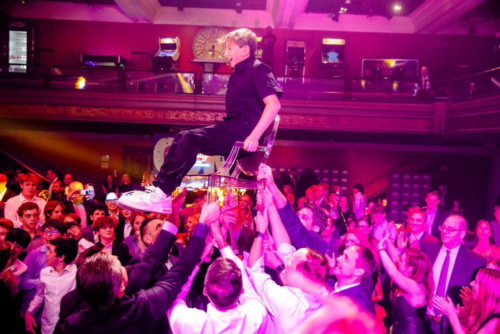 Person being lifted by crowd during an energetic indoor concert with purple lighting.