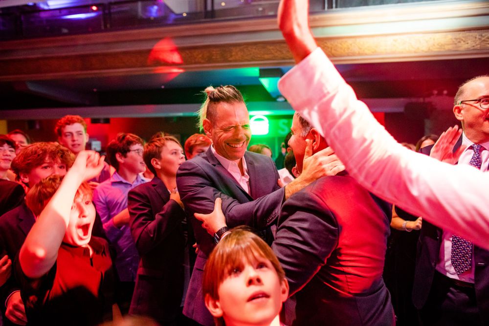Party goers dance enthusiastically under red and blue lighting at a vibrant club event.