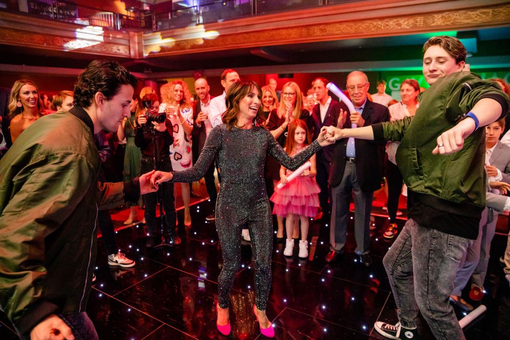 Attendees dance and socialize on a nightclub floor with dramatic red lighting overhead.