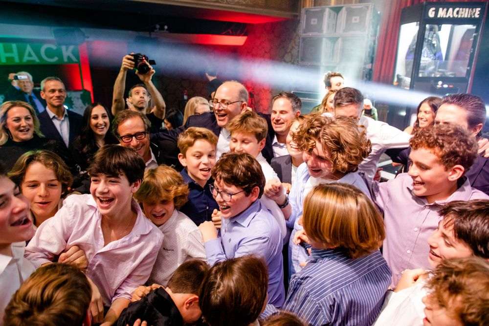 A crowded group of energetic attendees gather together at a nightclub event beneath colorful lighting.