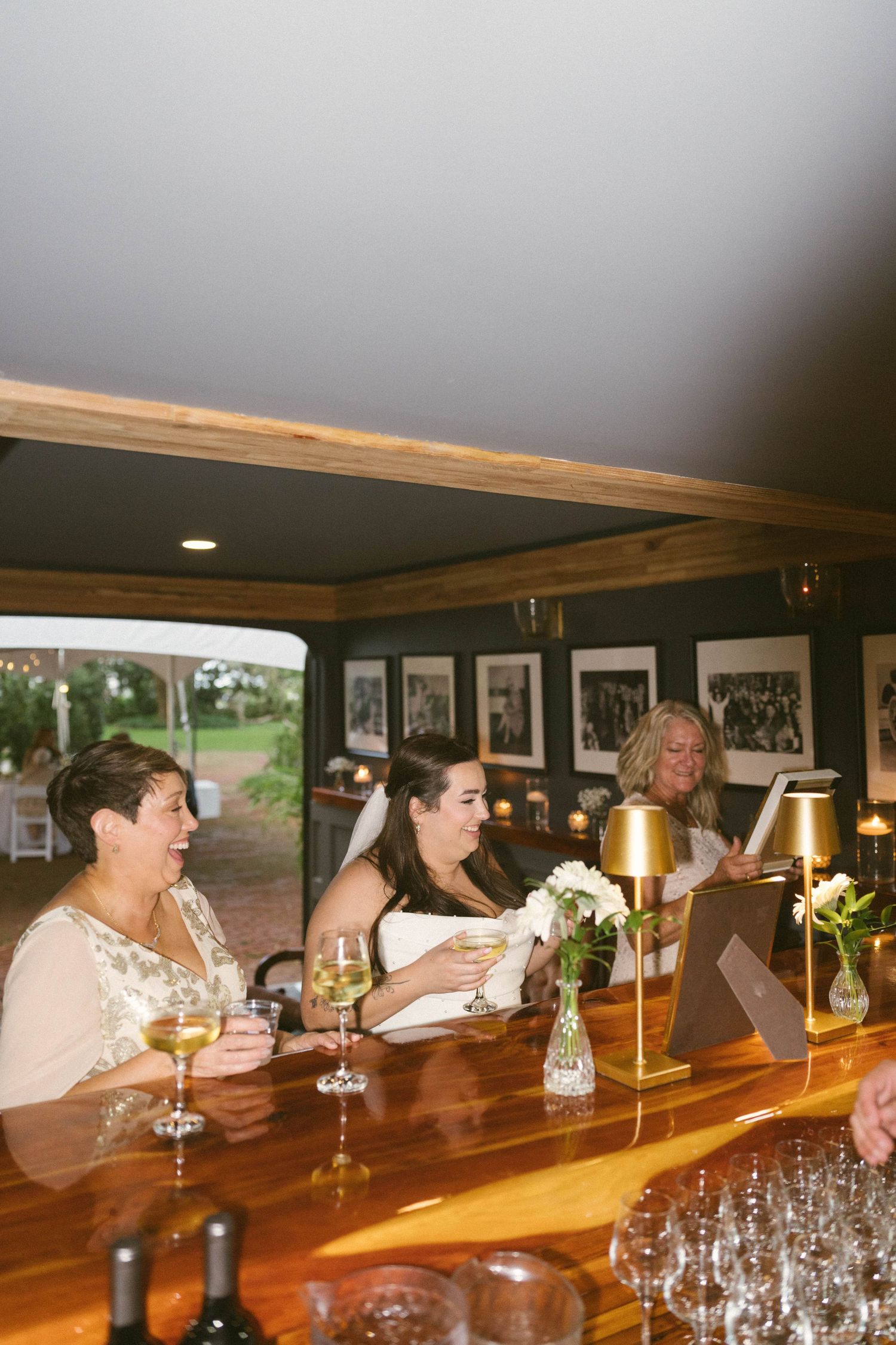Guests gathered at a wooden bar counter with wine glasses and beverages enjoying a social celebration.