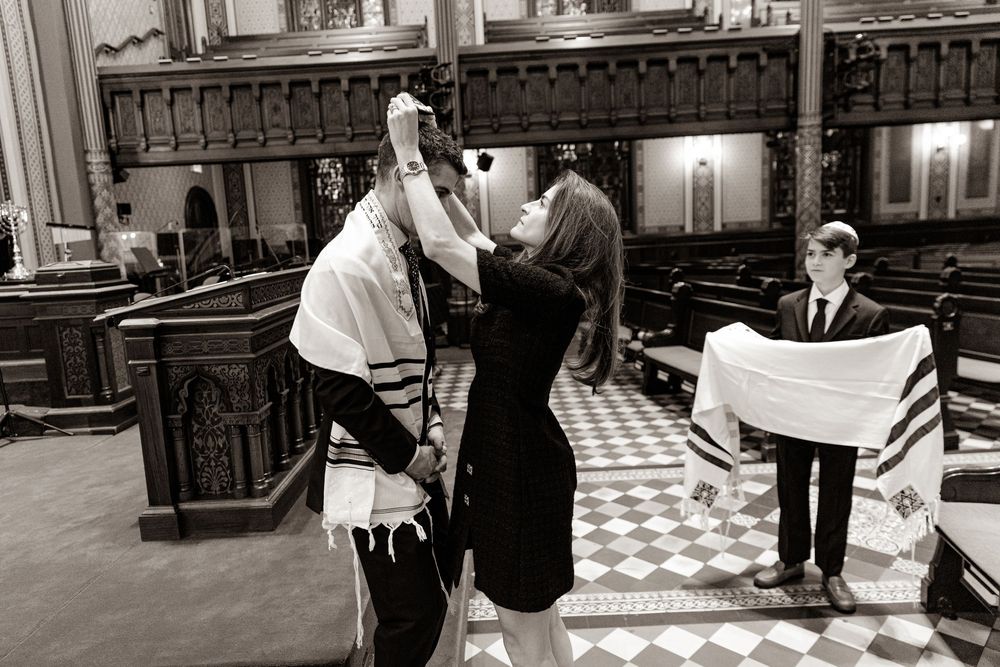 Young people in a synagogue during a bar mitzvah ceremony wearing traditional prayer shawls and kippot.