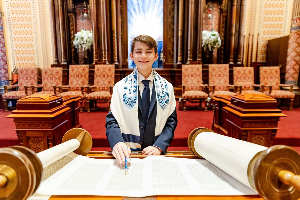 A person reading from an open Torah scroll at an ornate wooden podium in a grand synagogue.