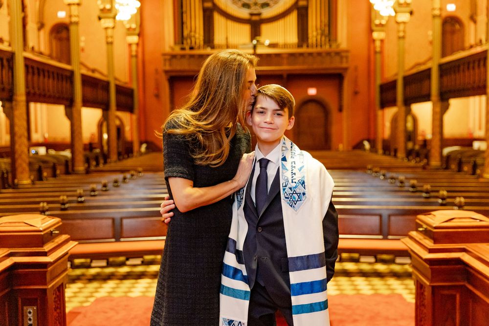 An intimate family moment captured in a beautiful synagogue with traditional Jewish prayer shawls and formal attire.