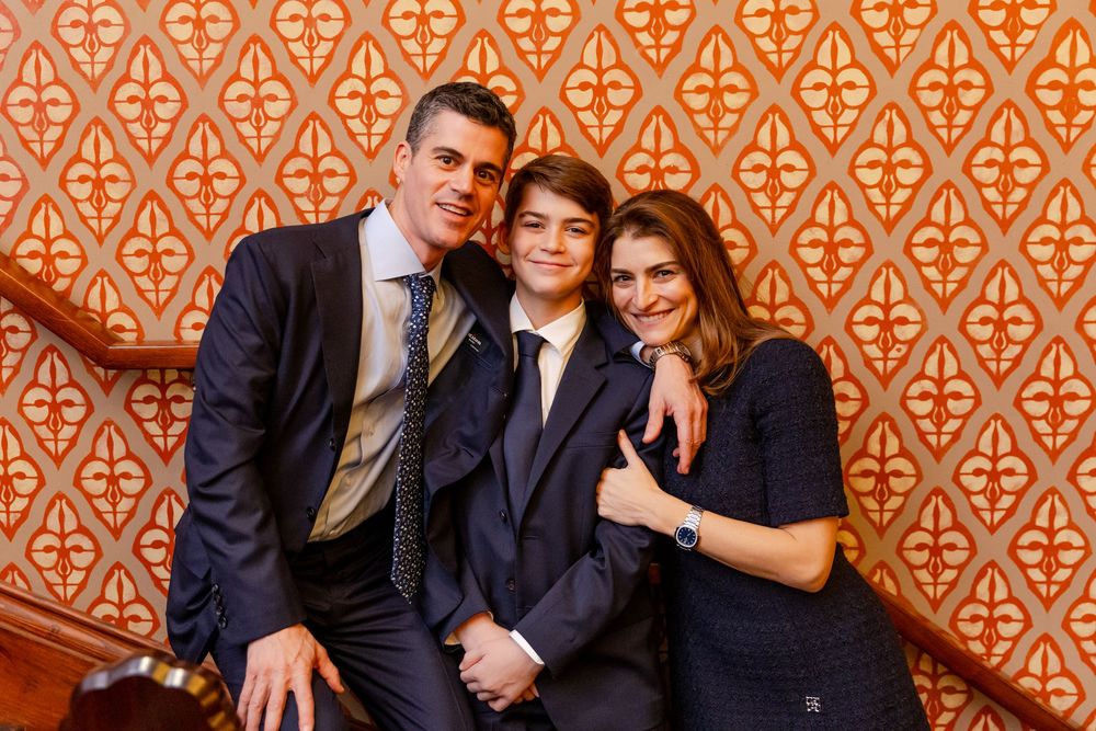 Group poses together in formal attire against an orange patterned wallpaper background.