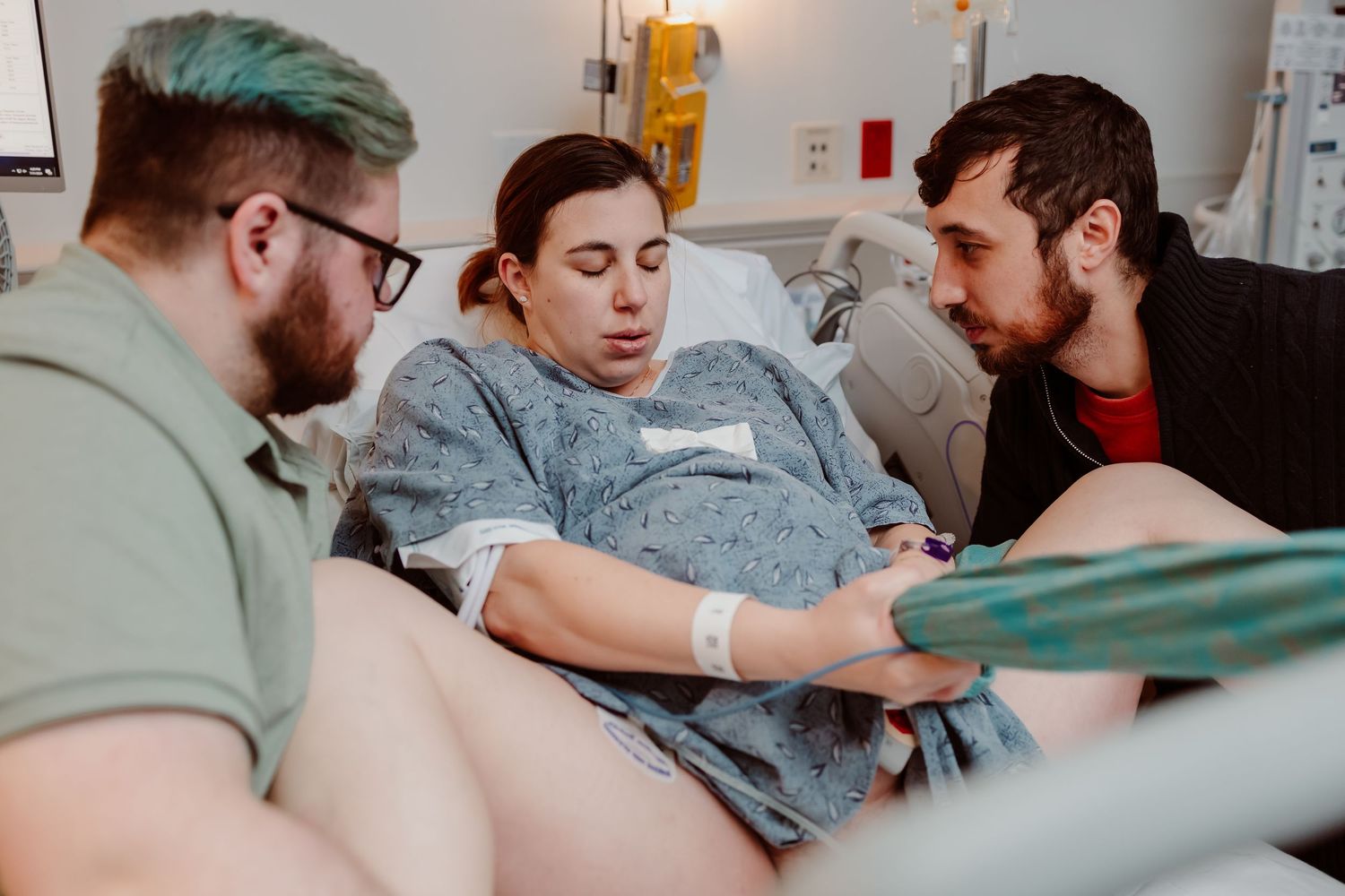 Medical professionals in scrubs and protective gear assist a patient during a hospital procedure.