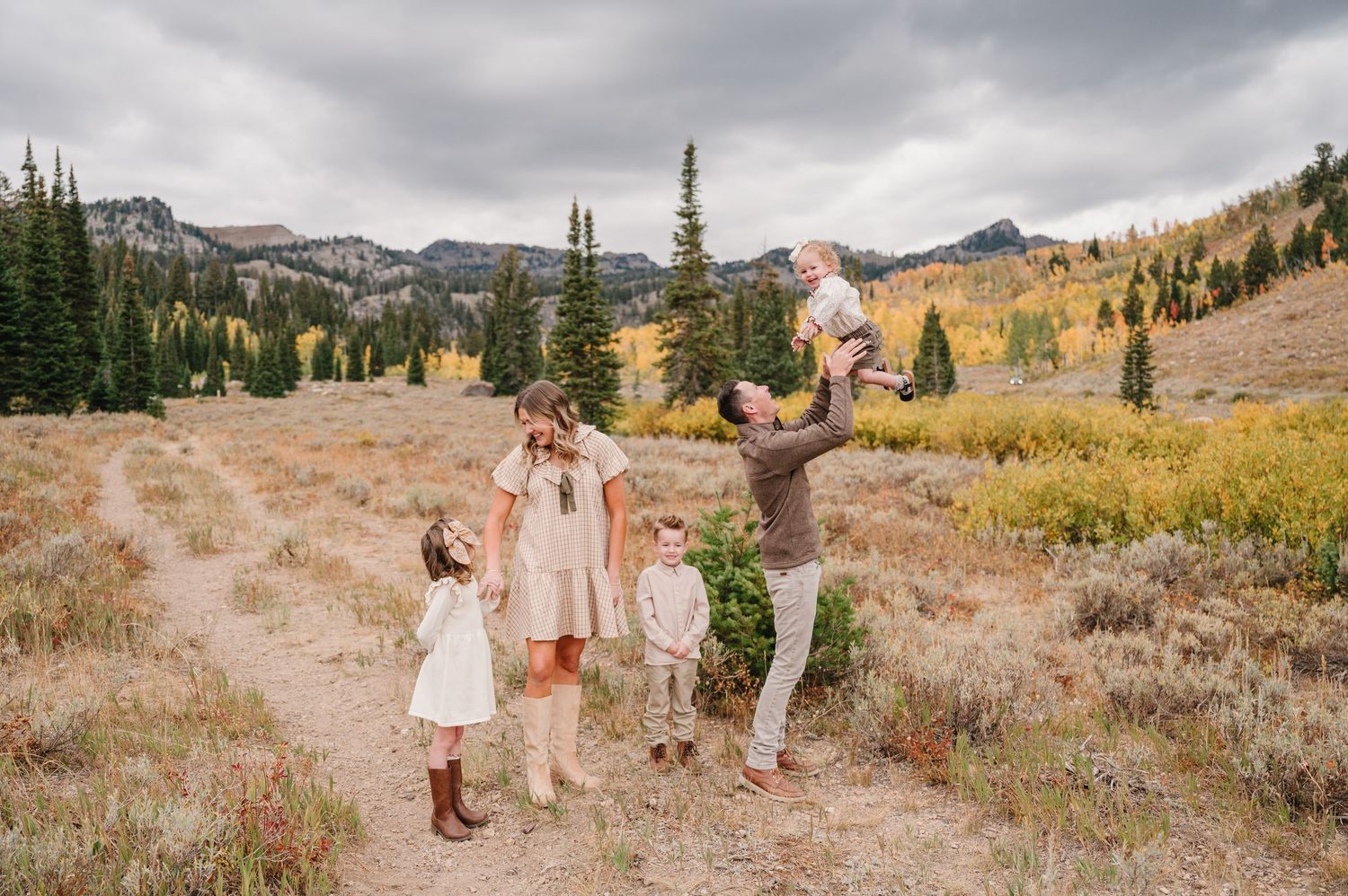 A couple in light colored attire poses together on a scenic mountain trail during autumn in Utah.