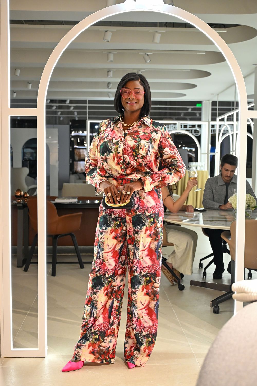 A person wearing a colorful floral robe poses in a modern office space with circular architectural details.