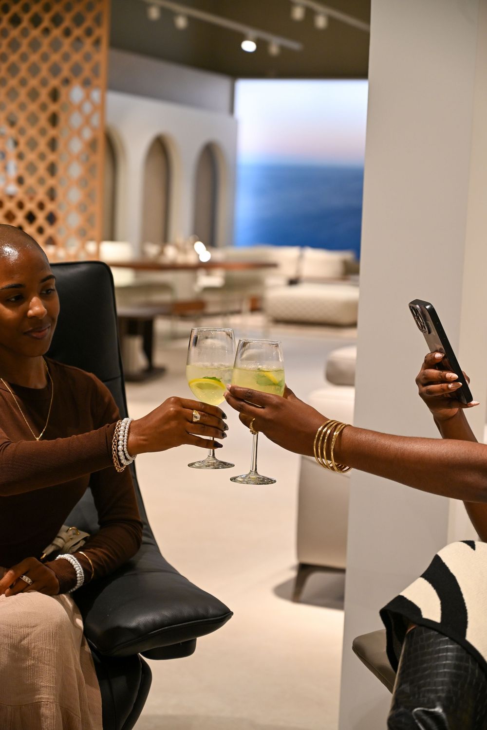 Hands holding cocktail glasses in a modern white interior space during a social gathering.
