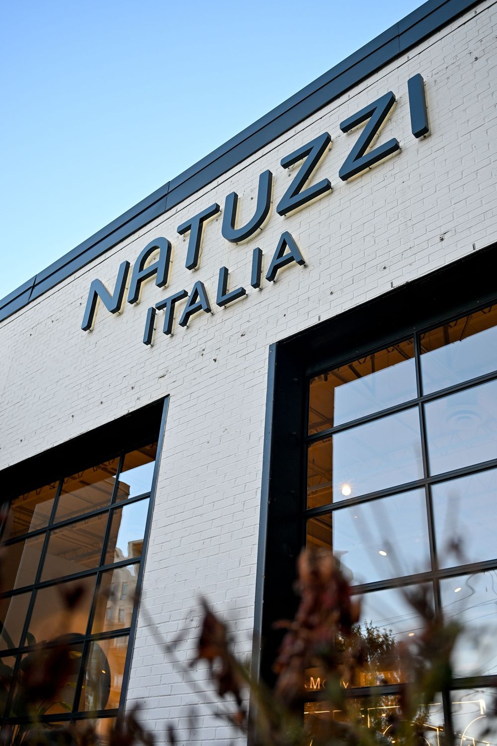 Exterior signage of Natuzzi Italia furniture store with modern white brick facade and window reflections.