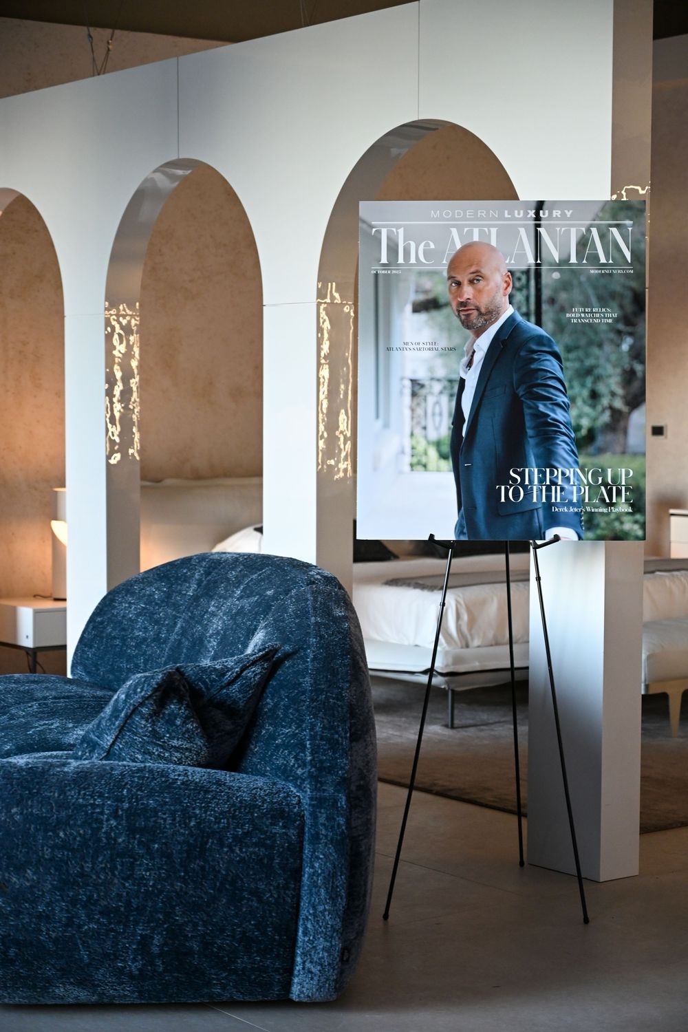 Interior gallery space with arched columns and a blue velvet couch displayed against white walls.