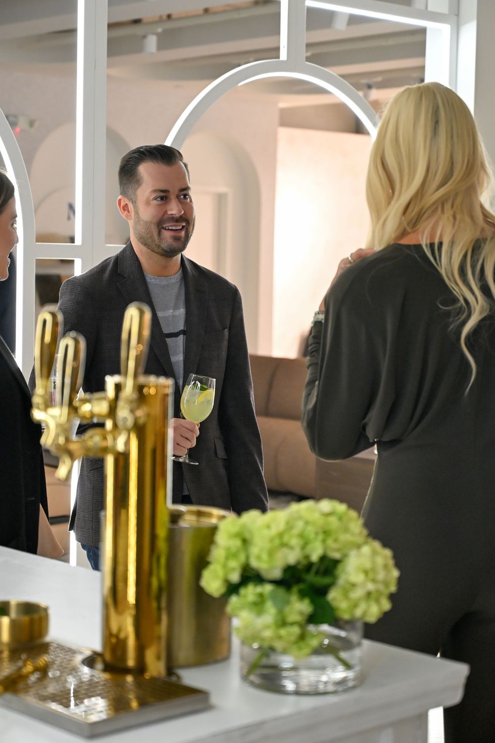 People gathered around a table with wine bottles and green grapes during a social event.