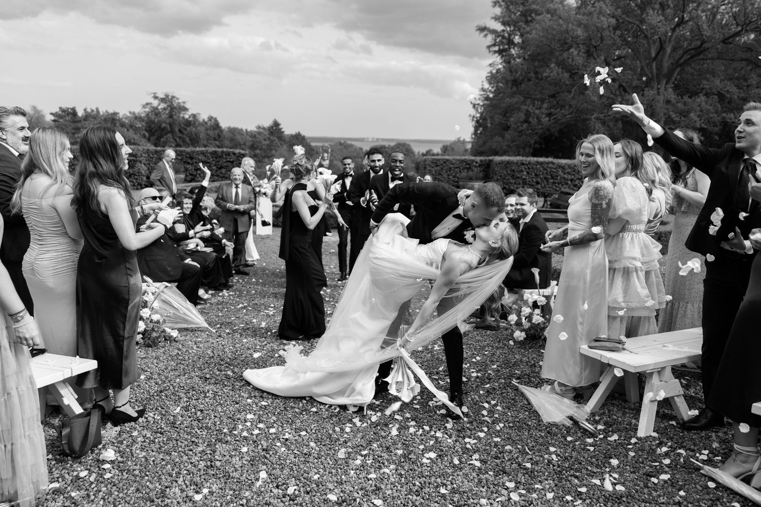 Black and white wedding party photo with bridal couple and attendants outdoors.