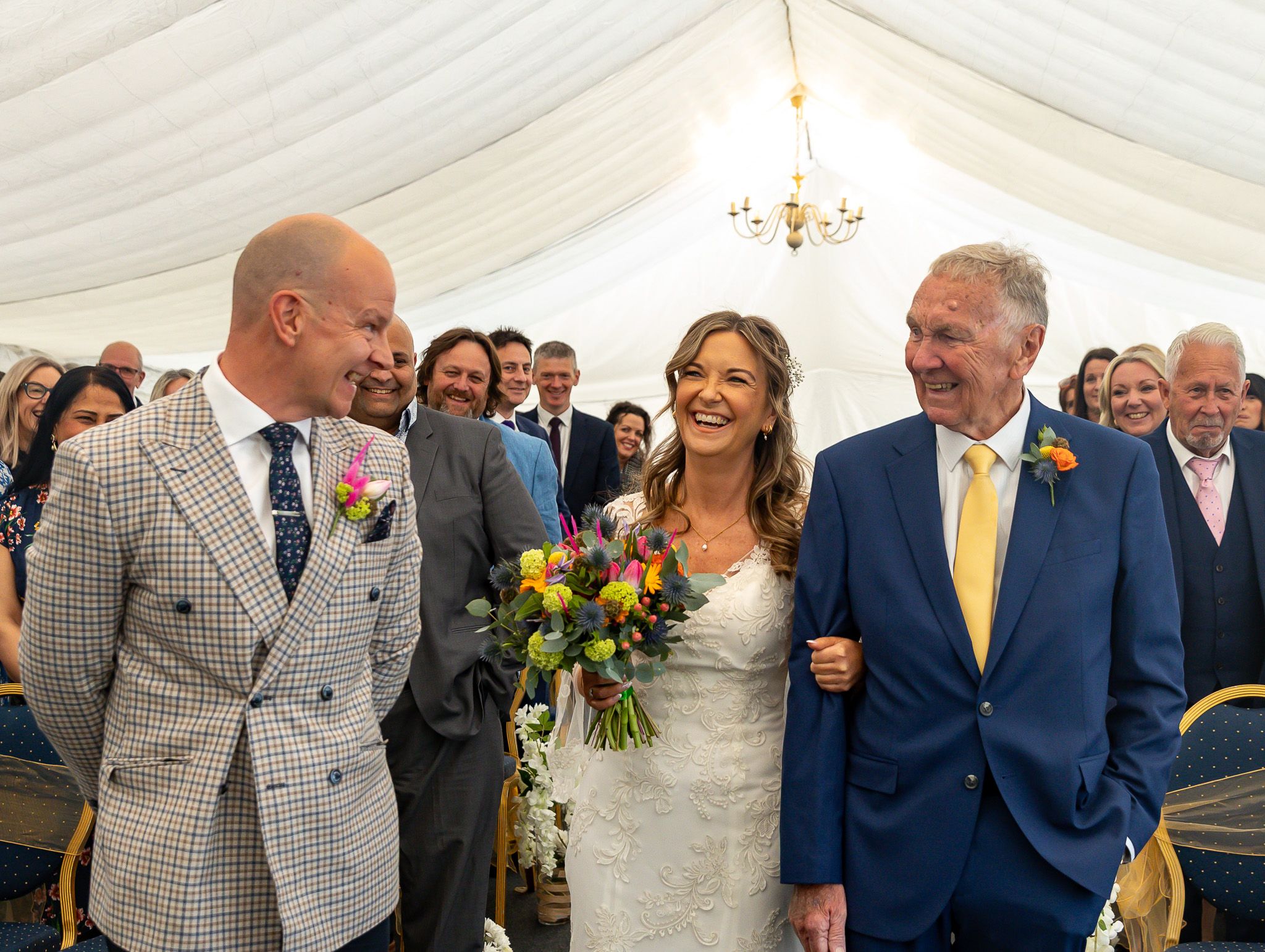 Wedding guests celebrate and laugh together under a white tent during an outdoor reception celebration.
