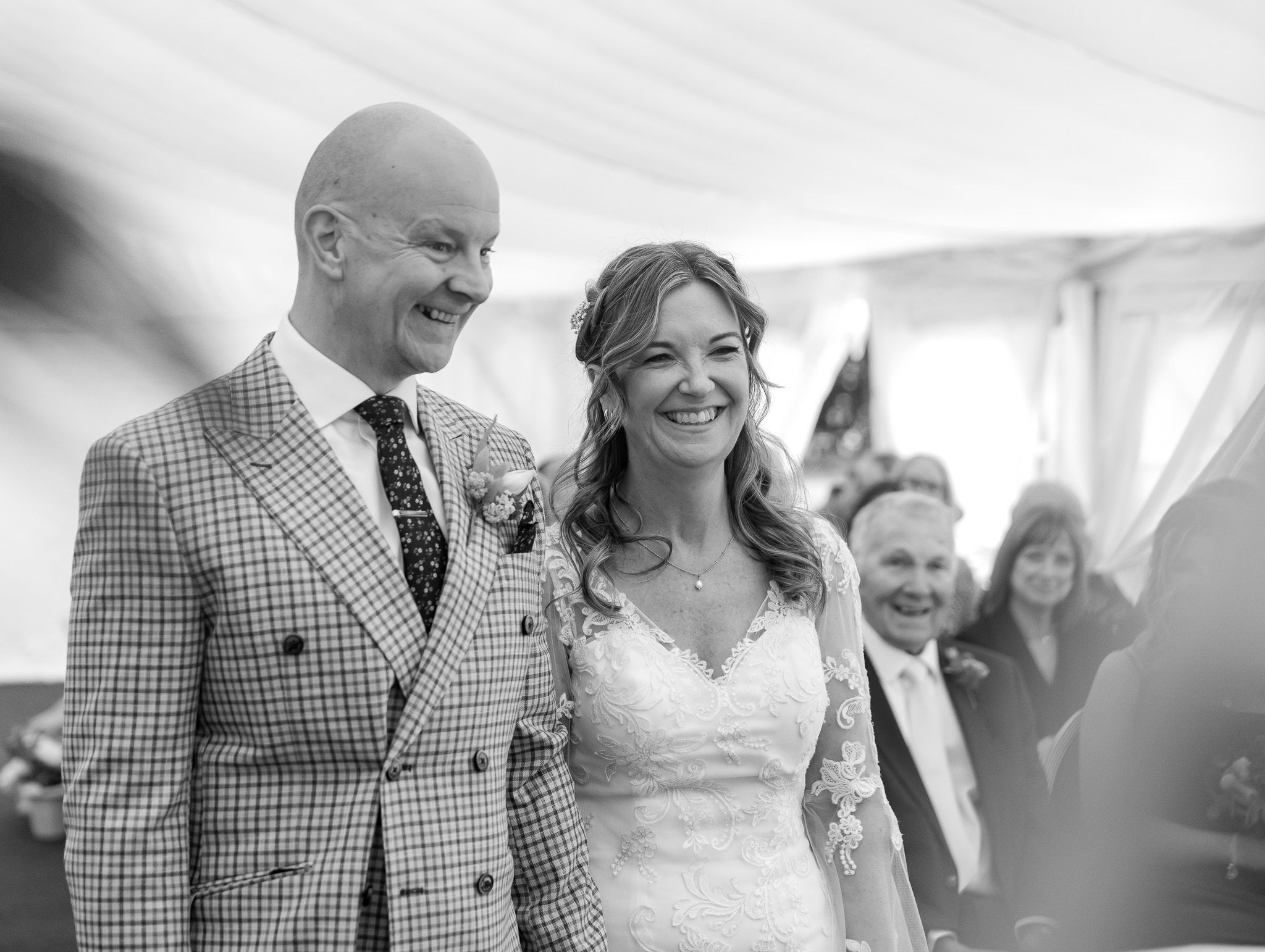 Happy couple laughing together during wedding reception in bright white tent venue.