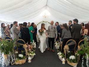 Wedding guests mingle and socialize under a large white tent decorated with floral arrangements and greenery.