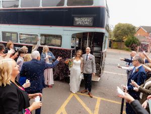 A group of wedding guests gather around a bus or coach in an outdoor setting during a celebration.