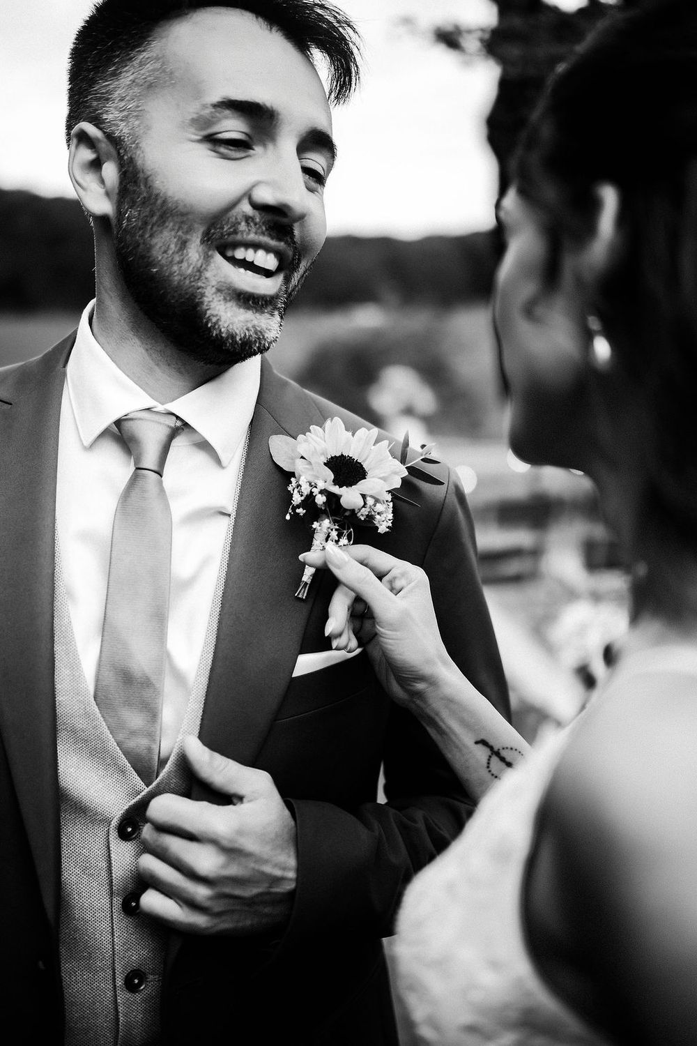 A black and white series of wedding photos showing a groom pinning a boutonniere flower to his lapel.