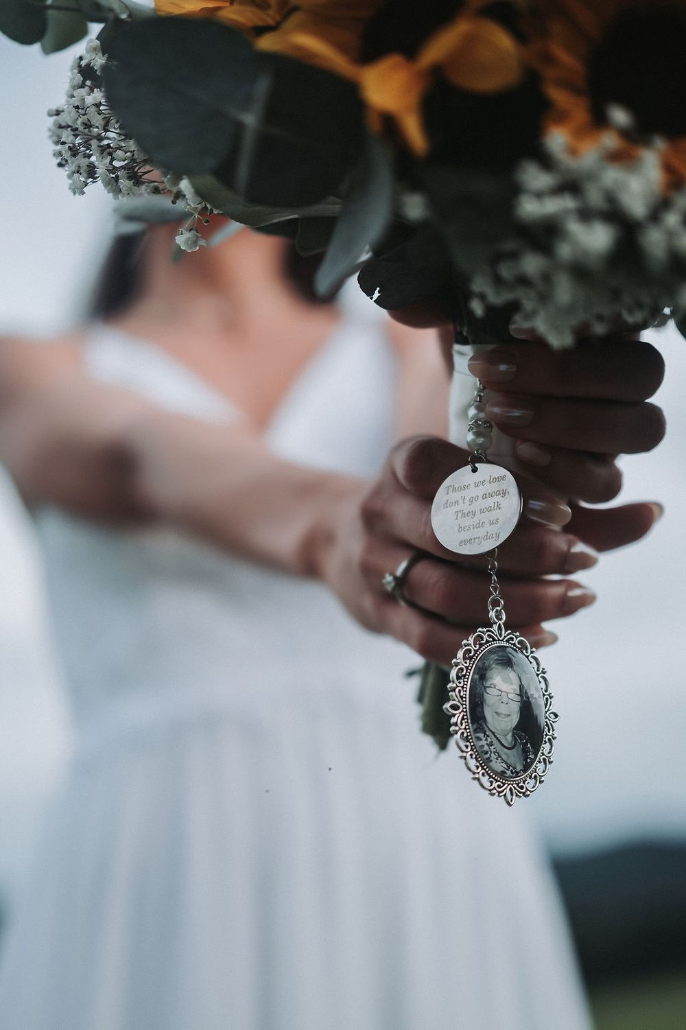 A bridal bouquet with a sentimental locket charm hanging from the stems against a white dress.