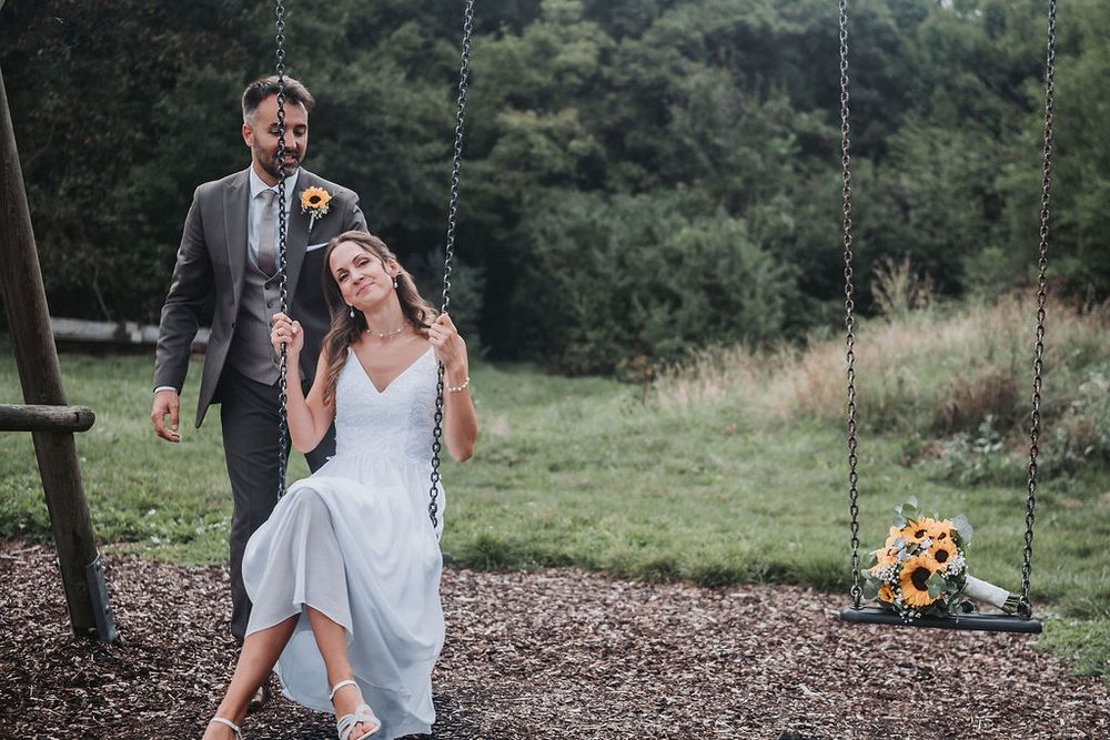 Joyful wedding couple dances and laughs together in a lush outdoor garden setting with natural greenery.