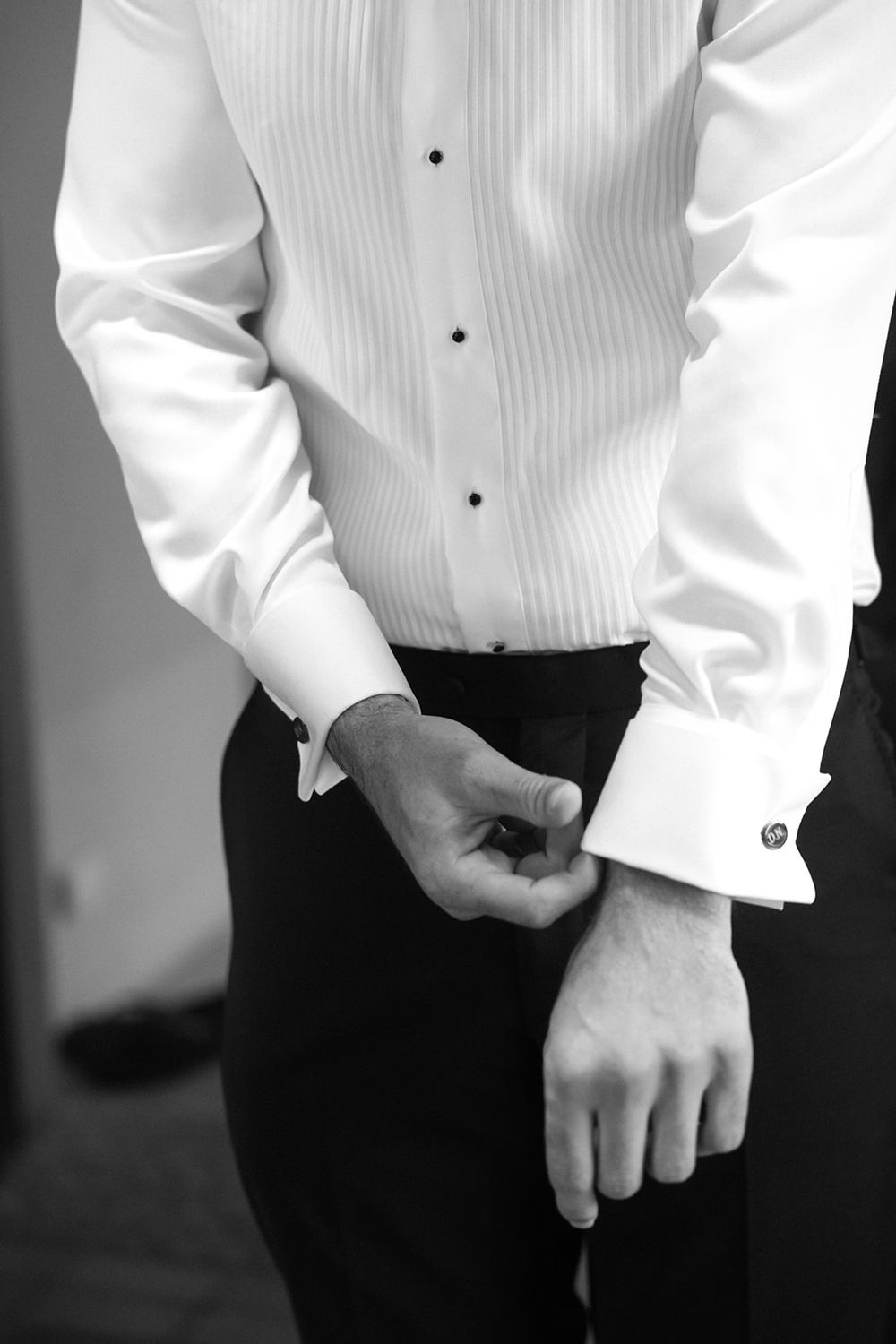 Close-up details of white tuxedo shirts and black formal wear in black and white photography.