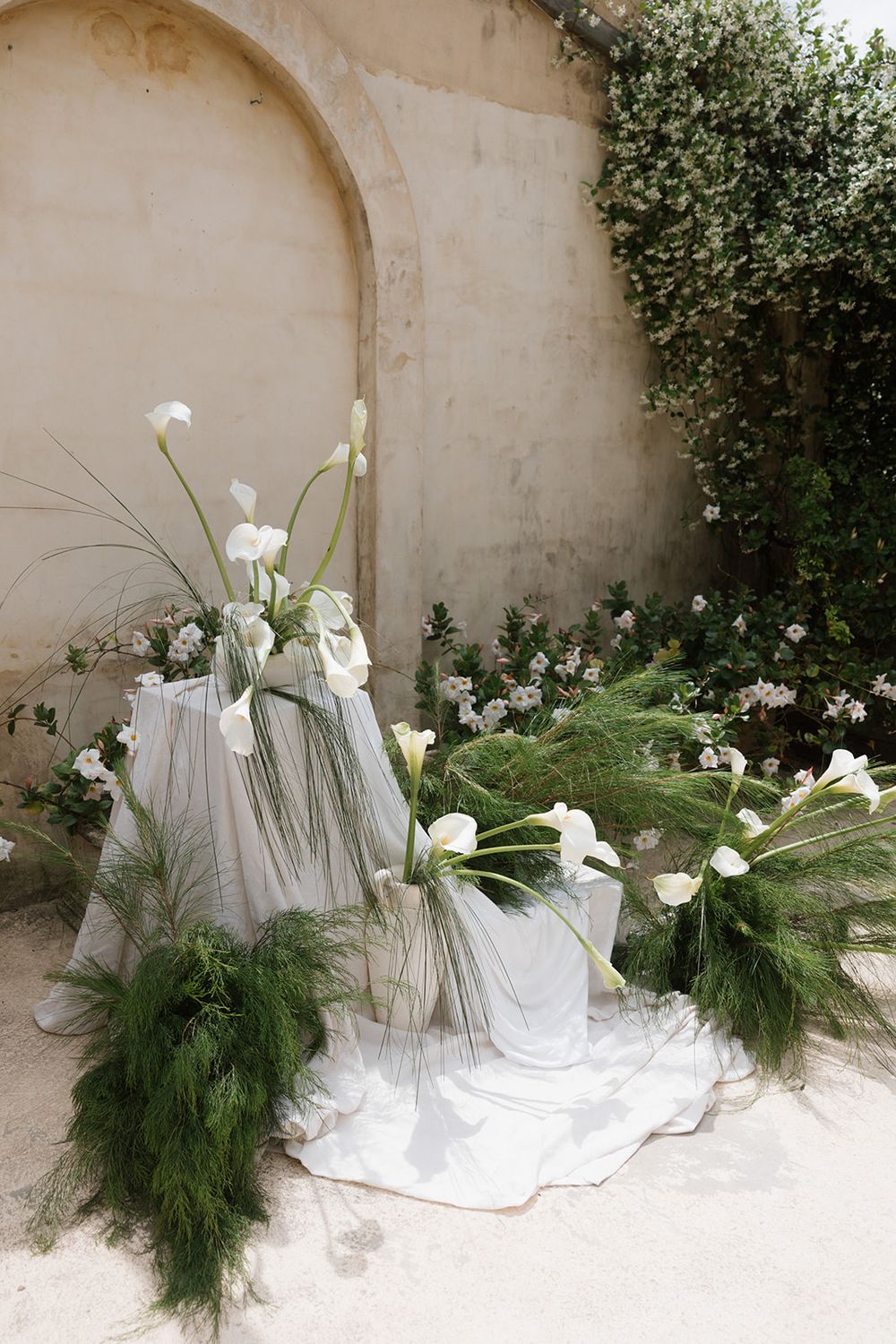 White calla lilies and greenery arranged against a neutral wall in a modern minimalist wedding installation.