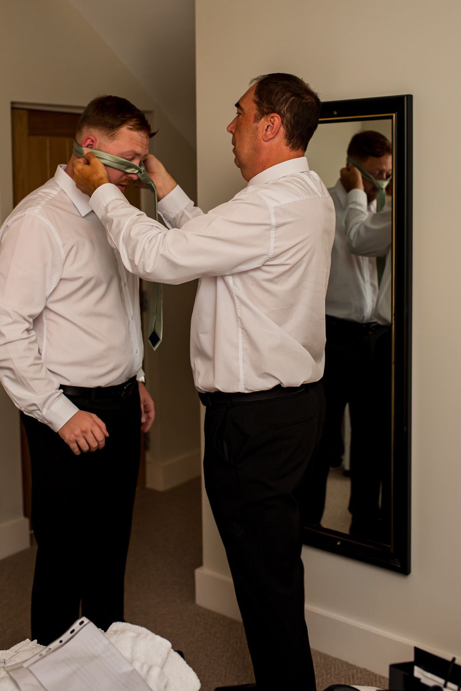 People in white dress shirts and black pants helping each other get ready in a room with mirrors.