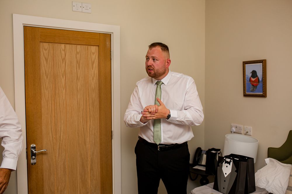 Two people in formal attire making final preparations in a beige-walled room.