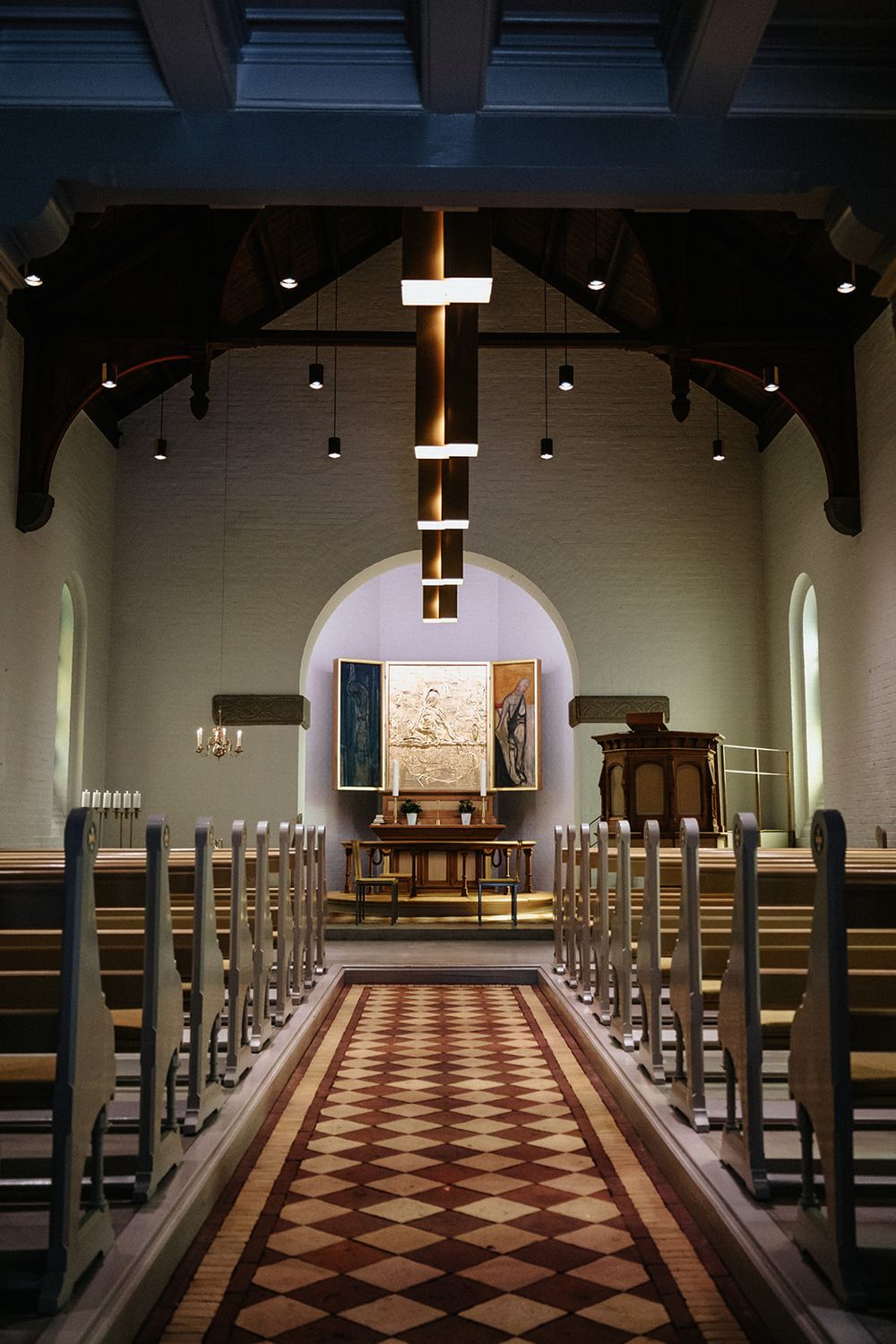 Interior view of a church sanctuary with wooden pews and a striking diamond-patterned floor leading to the altar.