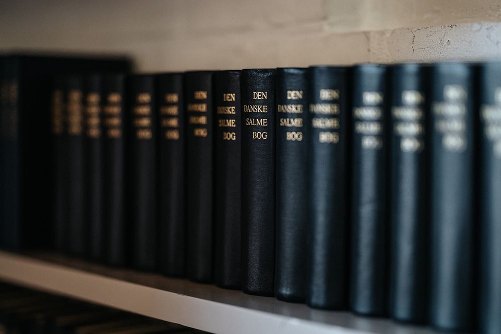 A row of dark hardcover books arranged on a wooden shelf in a library or study.